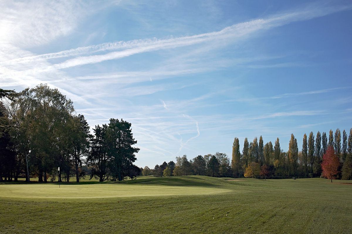 Fairway et green d'un golf du Nord sous un ciel bleu, rangée de peupliers au fond