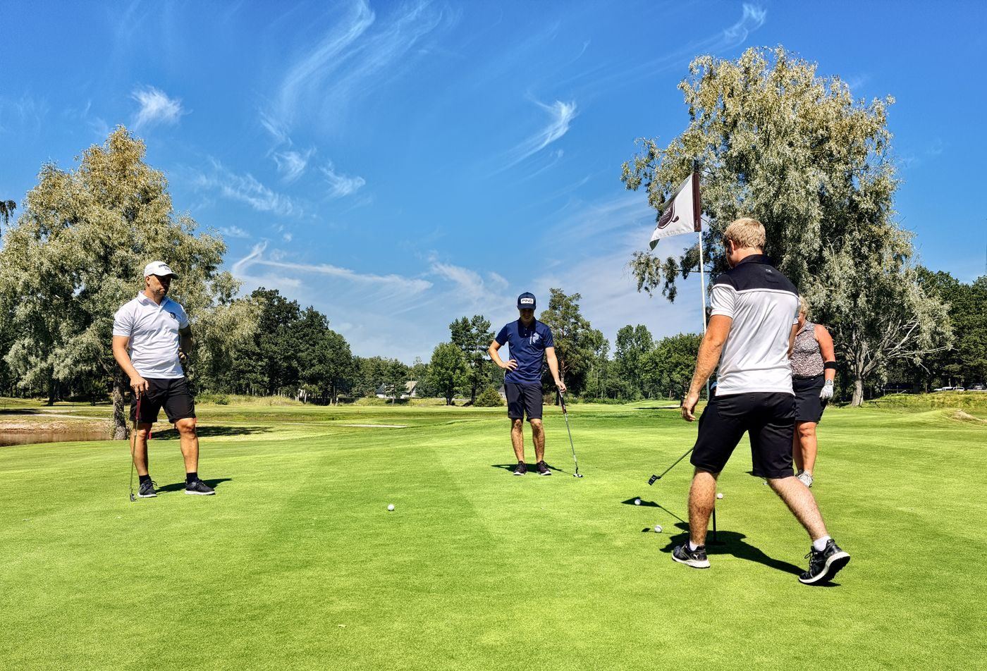 Quatre golfeurs sur un green ensoleillé, le drapeau planté près du trou