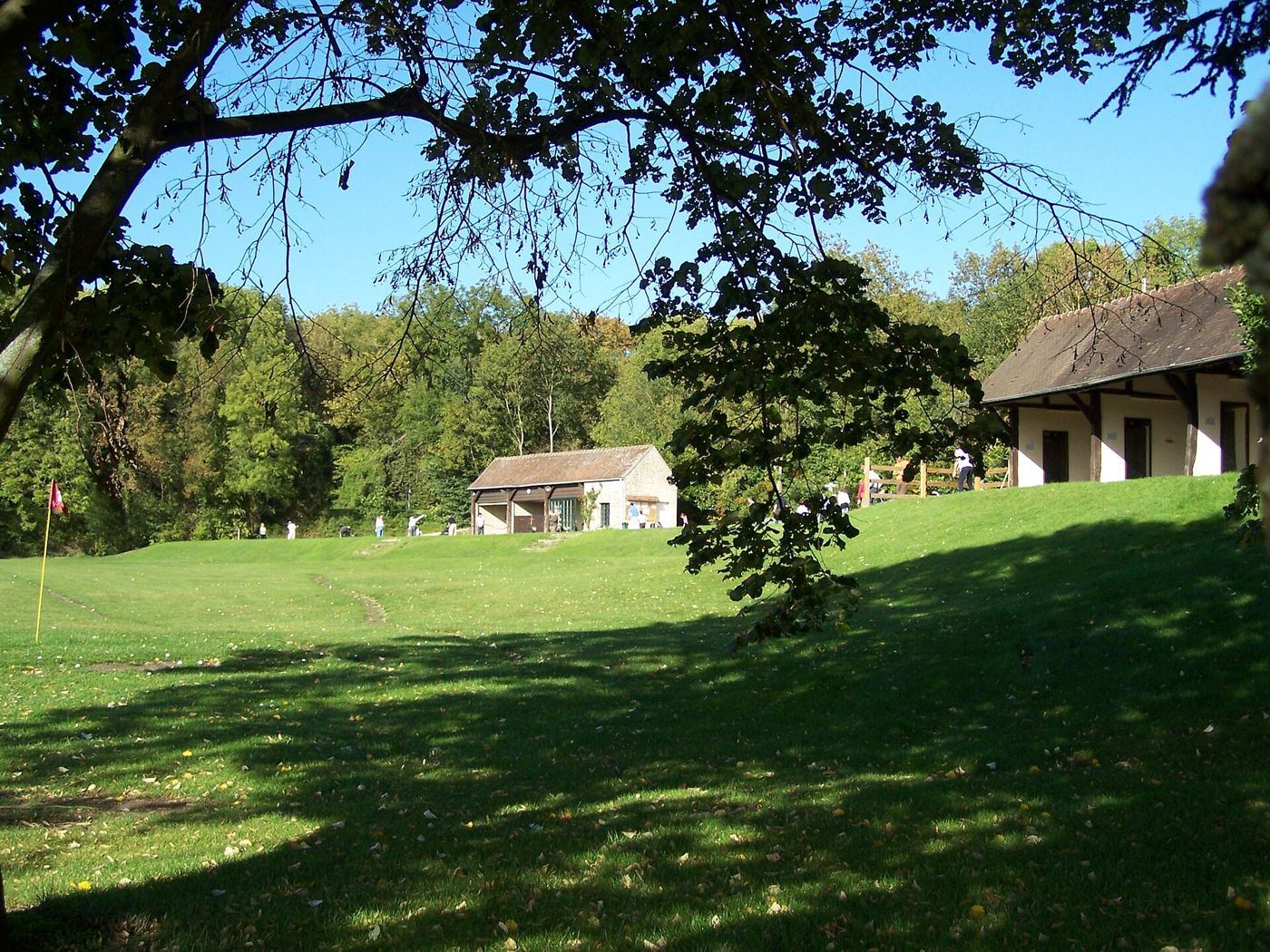Practice du golf de Saint-Nom-la-Bretèche sous les arbres, joueurs à l'entraînement devant les abris